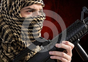 foreground of soldier side-face, with the face covered and weapon in his hands.red and black backgro