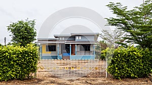 Foreground view looking through a wall of hedges to a modern Thai style house