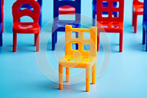 In the foreground, a yellow plastic chair, followed by another blue and red chairs