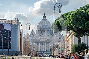 Foreign tourists strolling and being photographed in Rome, Italy on a bright sunny day in front of the dome of the main Catholic c