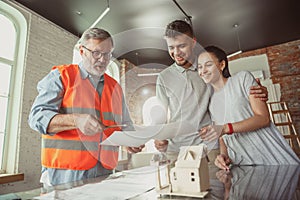 Foreman or achitect shows house, office or store design plans to a young couple