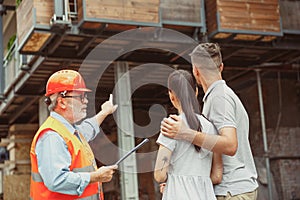 Foreman or achitect shows house, office or store design plans to a young couple