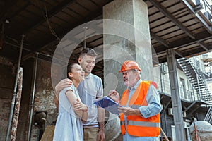 Foreman or achitect shows house, office or store design plans to a young couple