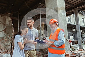 Foreman or achitect shows house, office or store design plans to a young couple