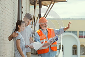 Foreman or achitect shows house, office or store design plans to a young couple