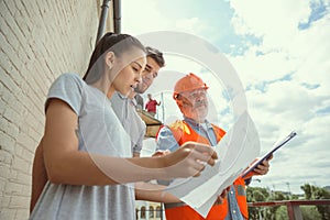 Foreman or achitect shows house, office or store design plans to a young couple