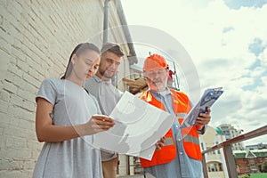 Foreman or achitect shows house, office or store design plans to a young couple