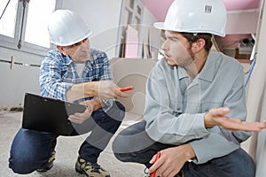 Foreman builder and construction worker with blueprint in indoor apartment