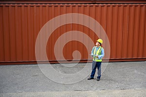 Foreman or Engineer wears yellow helmet and reflection shirt to control or check inventory details of containers box. Container