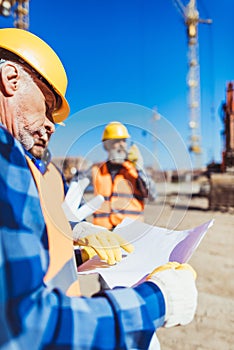 Foreman examining a building plan while standing at construction site