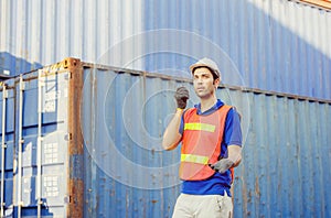 Foreman in hardhat and safety vest talks on two-way radio control loading containers box from cargo