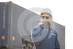 Foreman in hardhat and safety vest talks on two-way radio control loading containers box from cargo