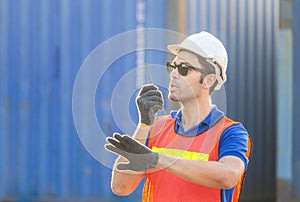 Foreman in hardhat and safety vest talks on two-way radio control loading containers box from cargo