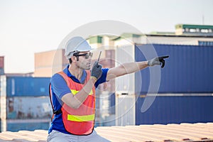 Foreman in hardhat and safety vest talks on two-way radio control loading containers box from cargo