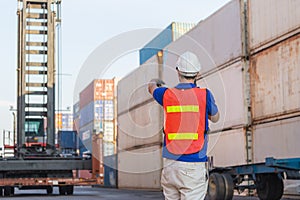 Foreman in hardhat and safety vest talks on two-way radio control loading containers box from cargo