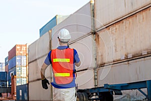 Foreman in hardhat and safety vest talks on two-way radio control loading containers box from cargo