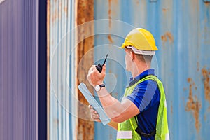 Foreman in hardhat and safety vest talks on two-way radio control loading containers box from cargo