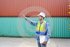 Foreman holding walkie talkie control loading Containers box from cargo freight ship for import export. Transportation logistic