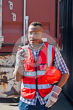 Foreman holding walkie- talkie for control working at Container cargo site. Handheld walkie talkie for outdoor