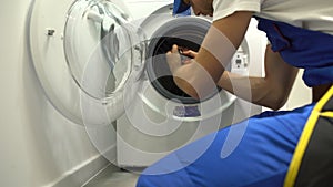 Foreman in uniform repairing washing machine using screwdriver, maintenance