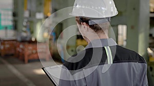 Foreman is wearing protective helmet and walking in a workshop during working day, monitoring labourers