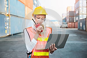 Foreman woman worker working checking at Container cargo harbor holding laptop computer and radio walkie-talkie to loading