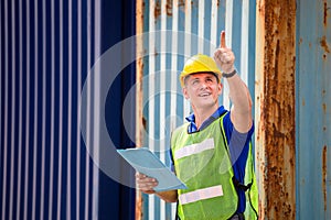 Foreman worker in hard hat and safety vest smiling and pointing control loading containers box from cargo
