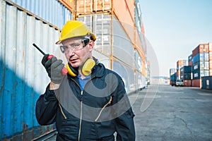 Foreman worker working checking at Container cargo harbor holding radio walkie-talkie to loading containers. Dock male staff