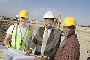 Foreman And Workers With Blueprint At Site