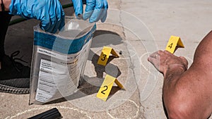 forensic inspector collecting firearm shells at a crime scene with a dead male person lying on the ground