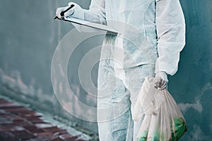 Forensic investigator collecting evidence on a murder scene on a street holding a plastic bag and wearing a hazmat suit