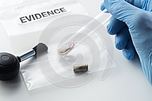 Forensic scientist`s hand holding glass tube over evidence bag next to brush