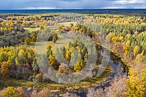 Forest in autumn colors. Colored trees and a meandering blue river. Red, yellow, orange, green deciduous trees in fall.