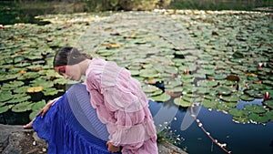 Forest fairy sitting lake covered water lilies close up. Dreamy woman posing