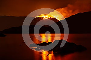 Forest fire at night reflecting in nearby lake.