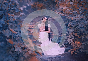 Forest goddess on stone steps, dreams with her eyes closed, dark-haired girl in long white dress, elegant golden wreath