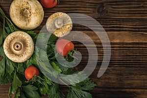 Forest mushrooms, two tomatoes and greens on a wooden background. Flat lay