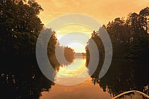 Forest reflection with boat on lake or river. Golden hour.