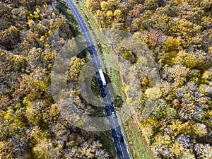 Forest road with white truck during Autumn. Aerial view road crossing a yellow and gold deciduous trees forest, Autumn