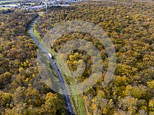 Forest road with white truck during Autumn. Aerial view road crossing a yellow and gold deciduous trees forest, Autumn