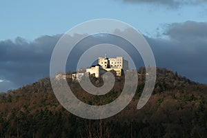 Forested landscape where Buchlov Castle stands on a hill. In the background is a sky with dark clouds