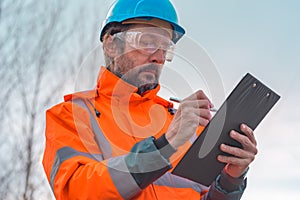 Forestry technician collecting data and writing at clipboard notepad