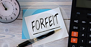 FORFEIT - word on a white sheet on the background of a calculator, alarm clock and pen