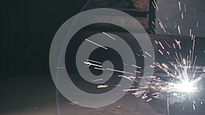 Forge workshop. Smithy. Worker in a welding hood helmet welds a part by electric welding. Sparks are reflected in the