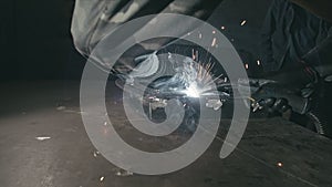 Forge workshop. Smithy. Worker in a welding hood helmet welds a part by electric welding. Sparks are reflected in the