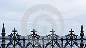 Forged black iron fence with decorative ornate pattern, blue sky background