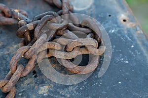 Forged old metal chain on the pier moored boat with peeling blue paint from the water, iron covered with rust