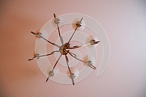 Forged vintage retro chandelier with eight shades hanging on the ceiling, on a white and pink background. View from below