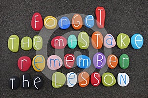 Forget the mistake, remember the lesson, inspirational quote with colored stones over black sand