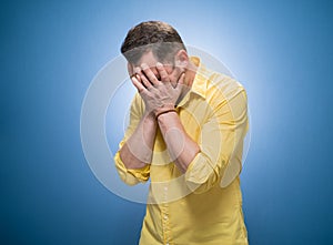 Forgetful man holding his hand on face over blue background, dresses in yellow shirt. Forget - forgot concept